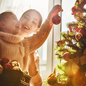 5 Ways to Save Money during the Holiday Season Mother and daughter hanging ornaments on a Christmas tree